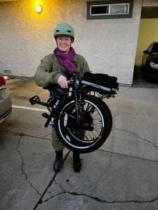 Heather, wearing a helmet, poses with folding bike, Zizzo