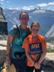 Tina and daughter Skylar. Yosemite is in the background. Tina wears a blue shirt, Skylar wears an orange shirt.